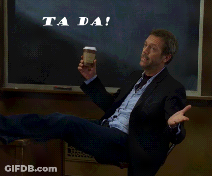 A Man In A Suit Sits In Front Of A Chalkboard That Says " Ta Da " GIF