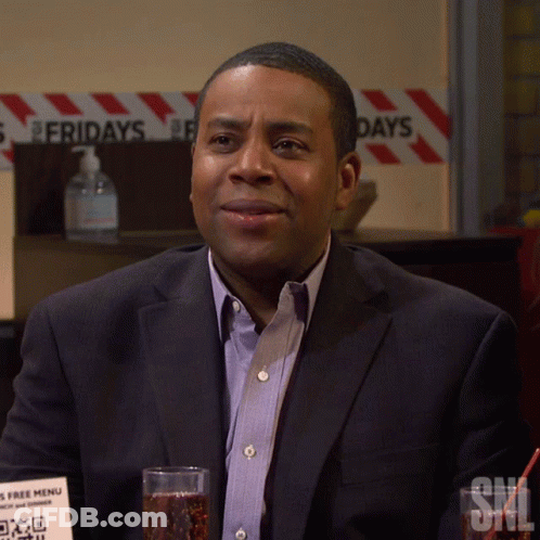 A Man In A Suit Sits In Front Of A Sign That Says Fridays On It GIF