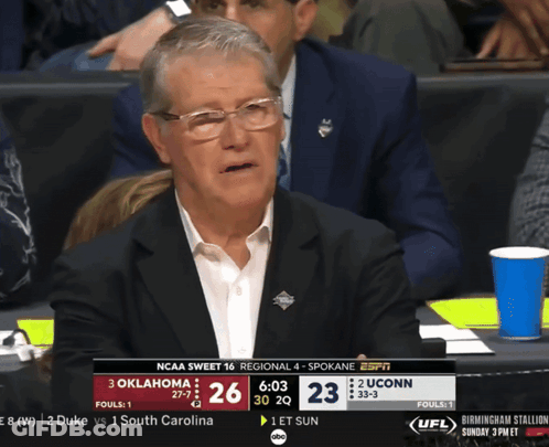 A Man In A Suit Sits In The Stands Watching A Ncaa Basketball Game Between Oklahoma And Uconn GIF