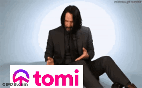 A Man In A Suit Sits Next To A Sign That Says Tomi GIF