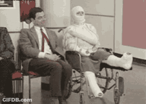 A Man In A Suit Sits Next To A Woman In A Wheelchair With A Cast On Her Leg . GIF