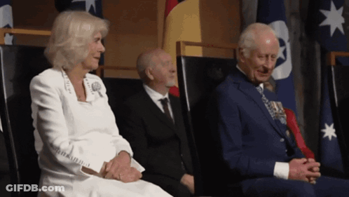 A Man In A Suit Sits Next To A Woman In A White Jacket GIF