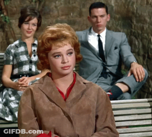 A Man In A Suit Sits On A Bench With Two Women Sitting Behind Him GIF