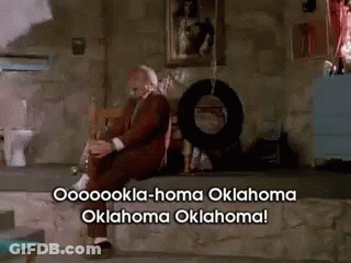 A Man In A Suit Sits On A Stone Ledge With Oklahoma Oklahoma Written On The Bottom GIF