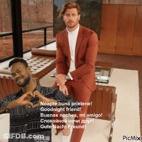 A Man In A Suit Sitting Next To Another Man Who Is Making A Heart With His Hands GIF
