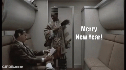 A Man In A Suit Sitting Next To Another Man With Merry New Year Written On The Screen GIF