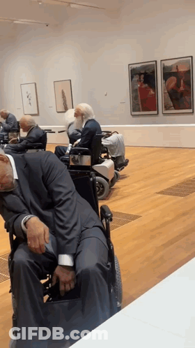 A Man In A Suit Sleeping In A Wheelchair In A Museum GIF