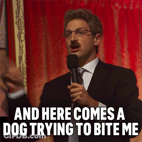 A Man In A Suit Speaking Into A Microphone With The Words And Here Comes A Dog Trying To Bite Me Below Him GIF