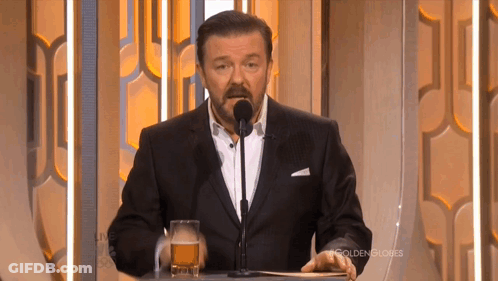 A Man In A Suit Stands At A Podium With A Glass Of Beer In Front Of Him GIF