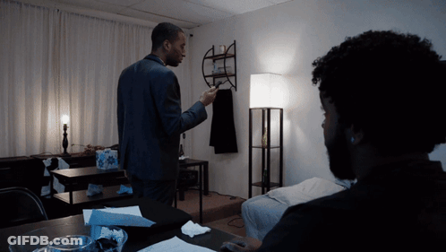 A Man In A Suit Stands In A Dark Room Talking To Another Man GIF