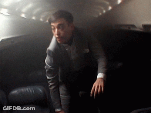 A Man In A Suit Stands In A Dark Room With His Hands On His Hips GIF