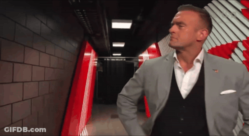 A Man In A Suit Stands In A Hallway With A Red And White Striped Wall Behind Him GIF