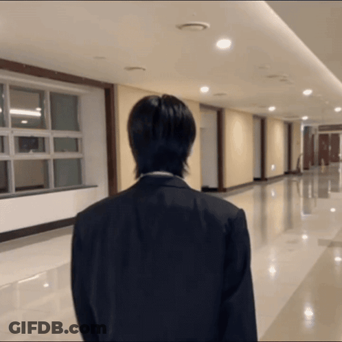 A Man In A Suit Stands In A Hallway With His Back To The Camera GIF