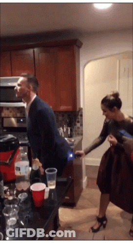 A Man In A Suit Stands In A Kitchen With A Woman Standing Behind Him GIF