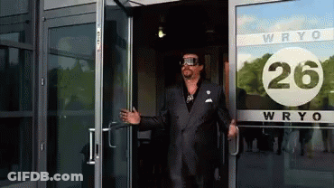 A Man In A Suit Stands In Front Of A Building That Says Wryo 26 GIF