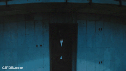 A Man In A Suit Stands In Front Of A Building With The Number 11 On The Door GIF