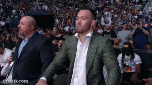 A Man In A Suit Stands In Front Of A Crowd GIF