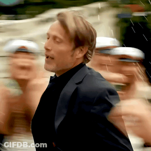 A Man In A Suit Stands In Front Of A Crowd Of People Wearing White Hats GIF