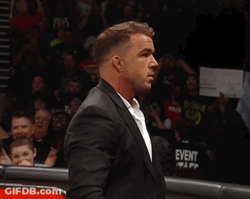 A Man In A Suit Stands In Front Of A Crowd With A Sign That Says Tna On It GIF