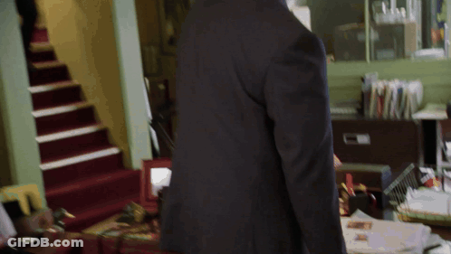 A Man In A Suit Stands In Front Of A Desk With Papers On It GIF