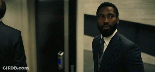 A Man In A Suit Stands In Front Of A Door GIF