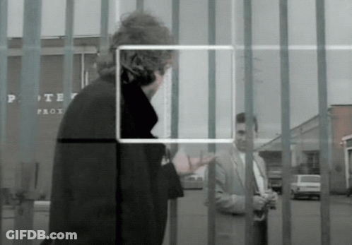 A Man In A Suit Stands In Front Of A Fence With A Sign That Says Porter Prox GIF
