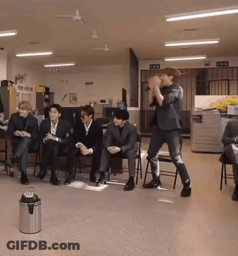 A Man In A Suit Stands In Front Of A Group Of People Sitting In Chairs GIF