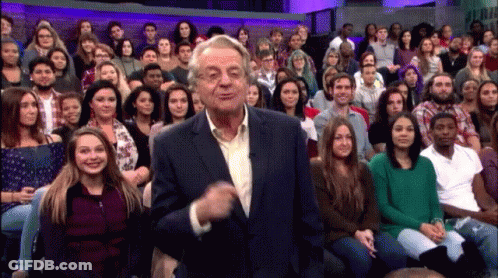 A Man In A Suit Stands In Front Of A Large Crowd GIF