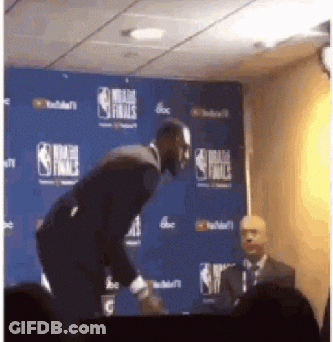 A Man In A Suit Stands In Front Of A Nba Finals Backdrop GIF