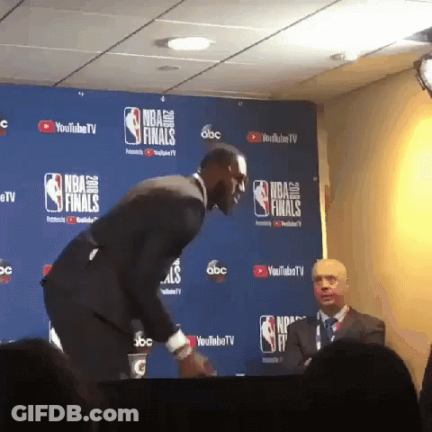 A Man In A Suit Stands In Front Of A Nba Finals Sign GIF