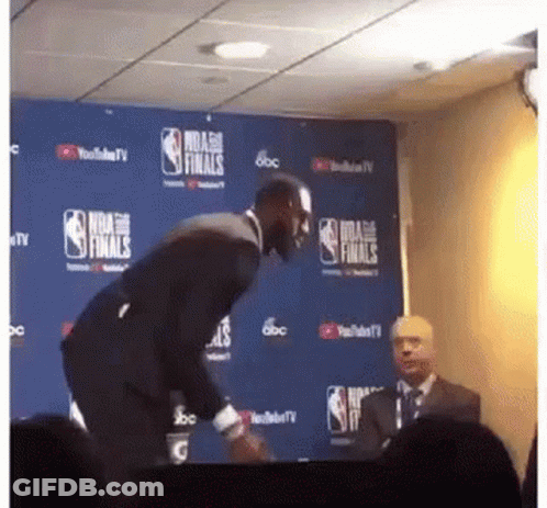 A Man In A Suit Stands In Front Of A Nba Finals Sign GIF