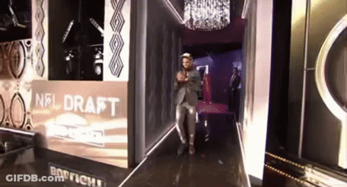 A Man In A Suit Stands In Front Of A Nfl Draft Sign GIF
