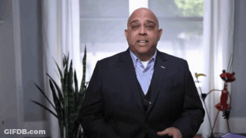 A Man In A Suit Stands In Front Of A Plant GIF