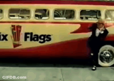 A Man In A Suit Stands In Front Of A Red And Yellow Bus That Says Flags GIF