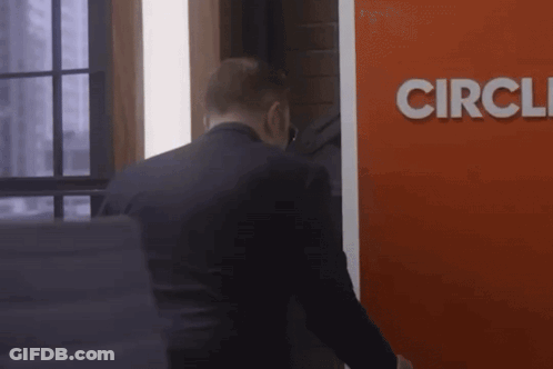 A Man In A Suit Stands In Front Of A Red Sign That Says Circle GIF
