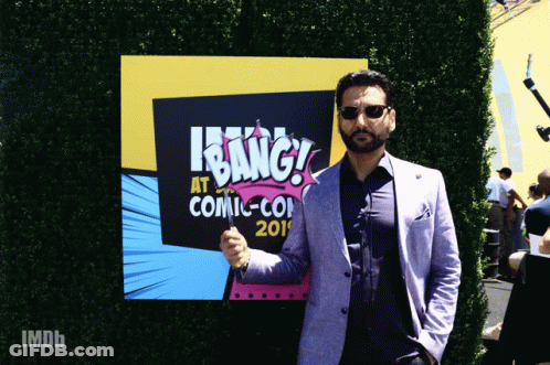 A Man In A Suit Stands In Front Of A Sign That Says " Bang " GIF