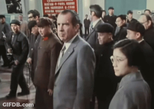 A Man In A Suit Stands In Front Of A Sign That Says ' Chinese ' On It GIF