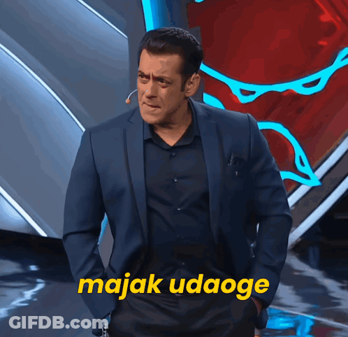 A Man In A Suit Stands In Front Of A Sign That Says Majak Udaogee GIF