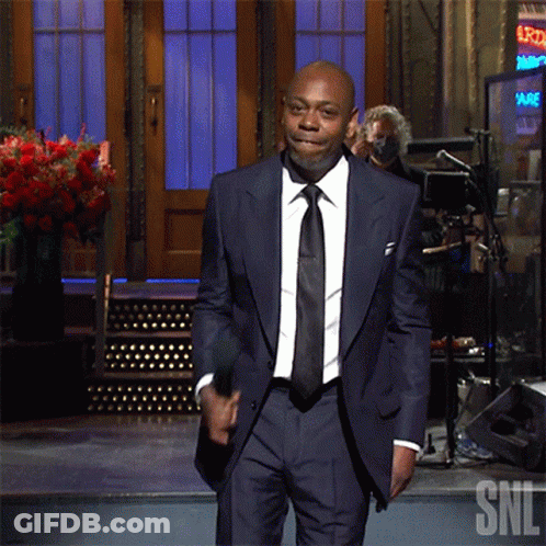 A Man In A Suit Stands In Front Of A Sign That Says Snl GIF