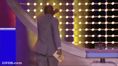 A Man In A Suit Stands In Front Of A Wall Of Lights Holding A Magazine GIF
