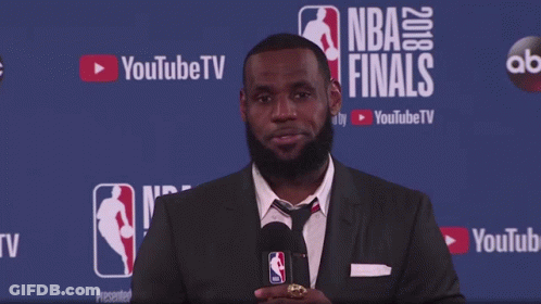 A Man In A Suit Stands In Front Of A Wall That Says Nba Finals GIF