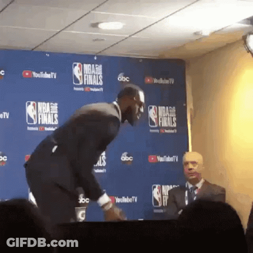 A Man In A Suit Stands In Front Of A Wall That Says Nba Finals On It GIF