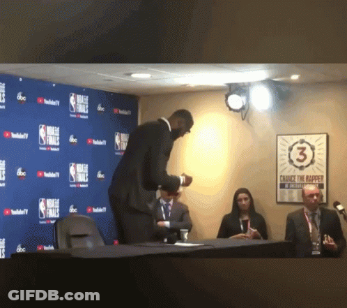 A Man In A Suit Stands In Front Of A Wall That Says Nba Finals On It GIF