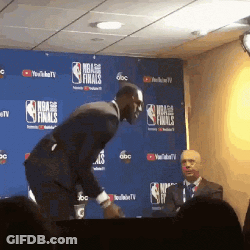 A Man In A Suit Stands In Front Of A Wall With Nba Finals Written On It GIF