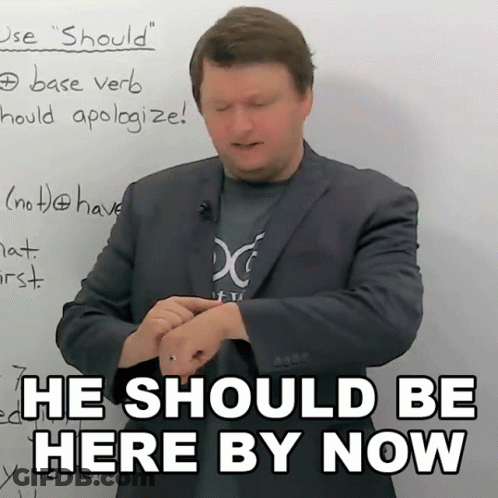A Man In A Suit Stands In Front Of A White Board With The Words He Should Be Here By Now GIF