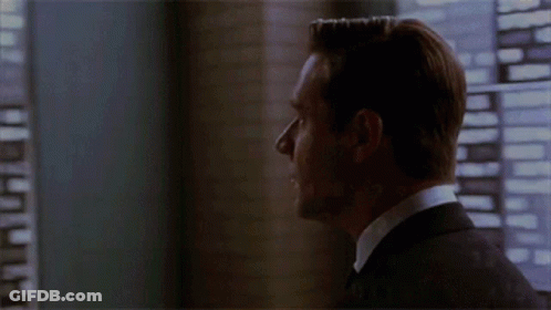 A Man In A Suit Stands In Front Of A Window Looking Out GIF