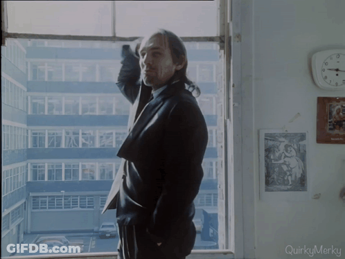 A Man In A Suit Stands In Front Of A Window With Quirkymerky Written On The Bottom GIF