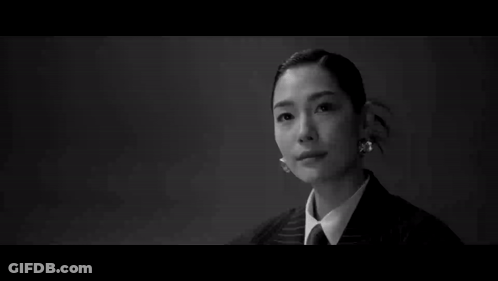 A Man In A Suit Stands In Front Of A Woman Sitting At A Table GIF