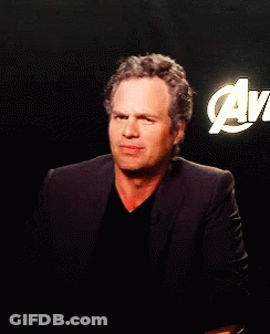 A Man In A Suit Stands In Front Of An Avengers Logo GIF