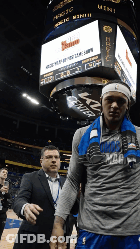 A Man In A Suit Stands Next To A Basketball Player In Front Of A Sign That Says Magic Wrap Up Post Game Show GIF